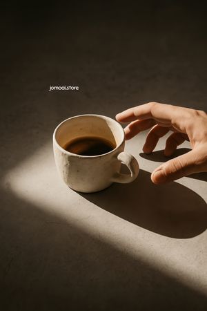 Hand reaching for ceramic coffee cup in warm sunlight