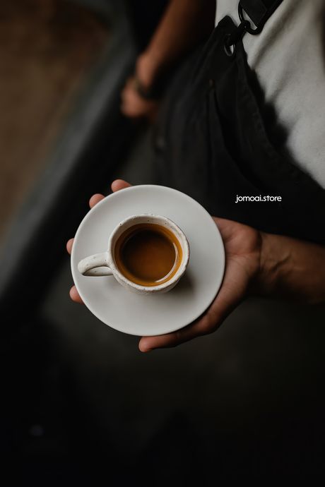 Hand holding espresso in handmade ceramic cup on saucer