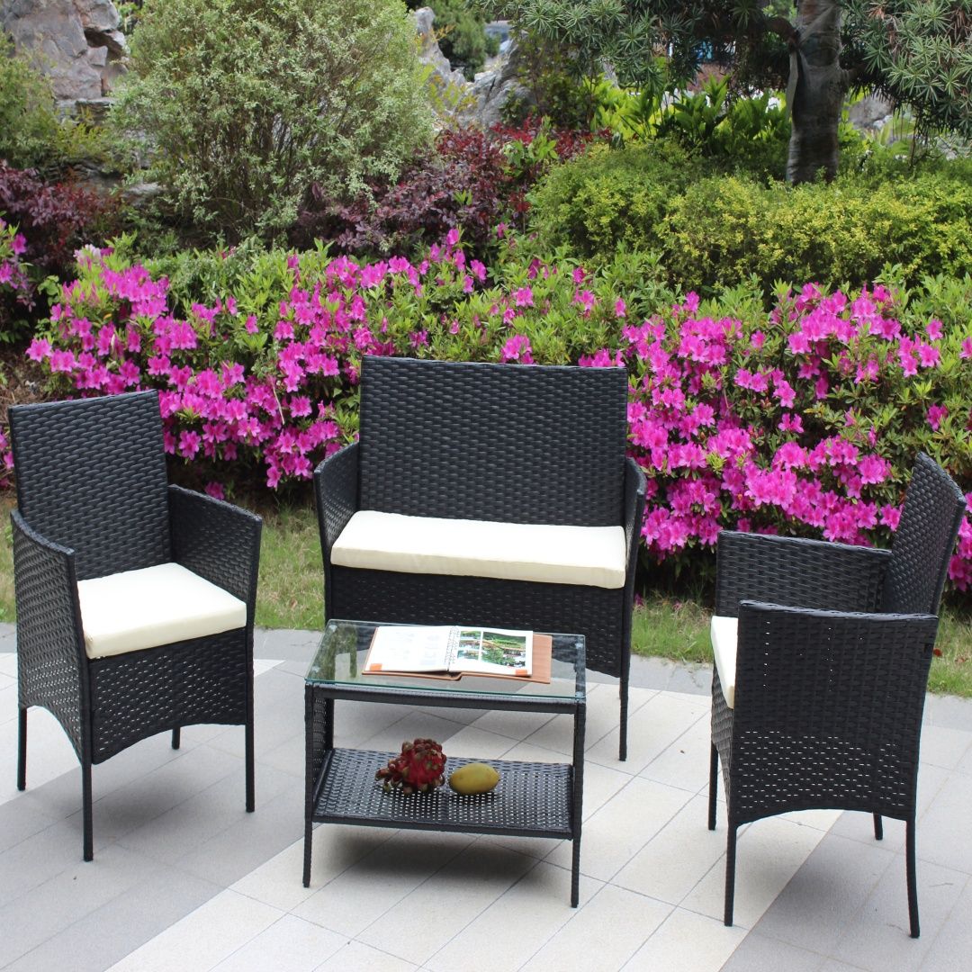 Four-piece wicker patio set with beige cushions in a garden