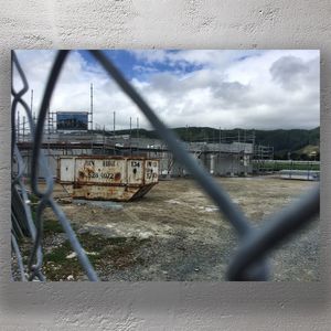Rusty Skip Bin at Construction Site Behind Fence with Scaffolding and Overcast Sky Photo Download