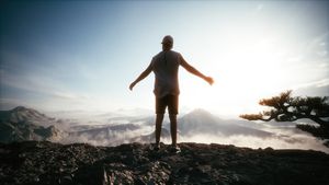 The concept of achieving success. Man standing on top of a mountain peak at sunset